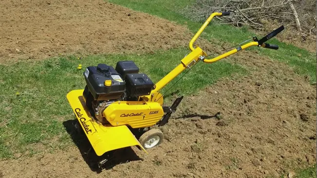 Yellow Cub Cadet garden tiller on freshly tilled soil with green grass in the background