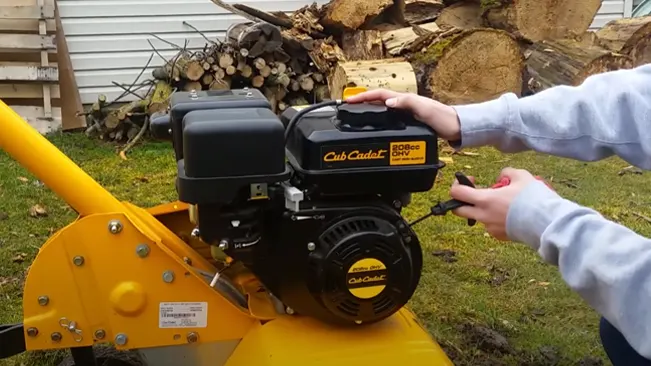 Hand adjusting a Cub Cadet wood chipper engine, with stacked wood in the background.