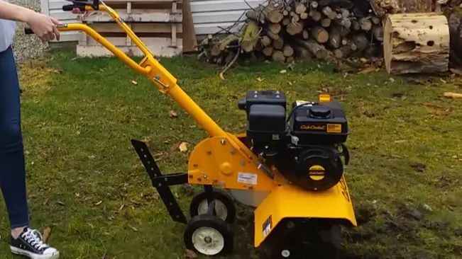 a person operating a yellow wood chipper in a yard, with stacked wood logs in the background.