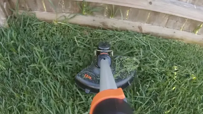 Person trimming grass near a wooden structure with a string trimmer
