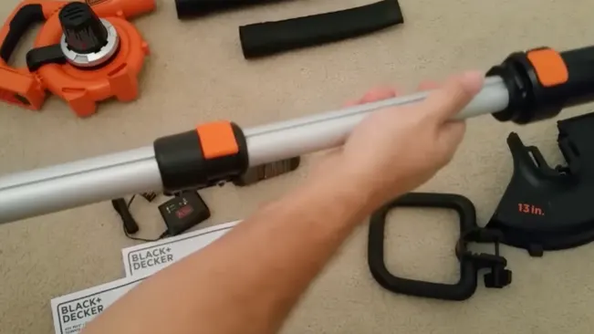 Person assembling a BLACK+DECKER string trimmer with various parts scattered around