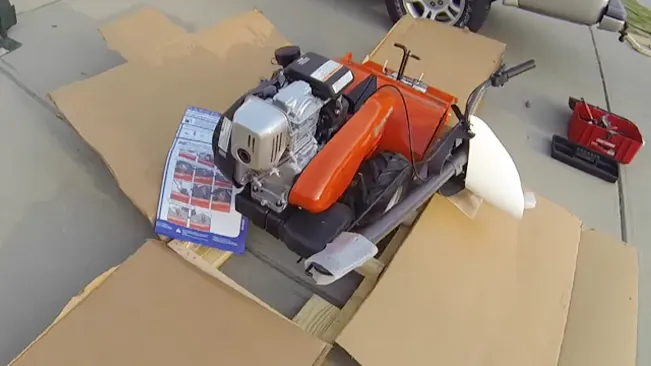 partially assembled orange and black motorcycle on cardboard with a toolkit nearby
