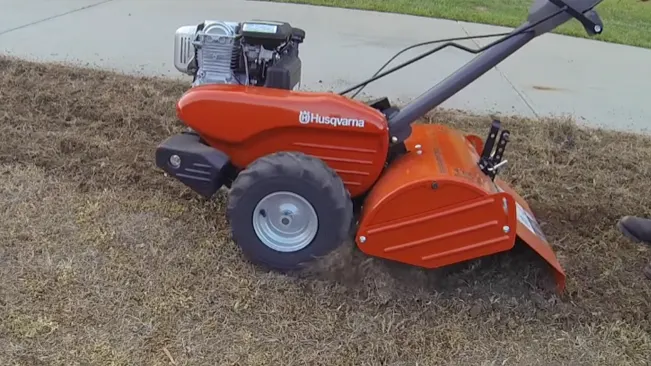 usqvarna tiller on a partially tilled grassy field, with the brand name “Husqvarna” visible on the body of the tiller.