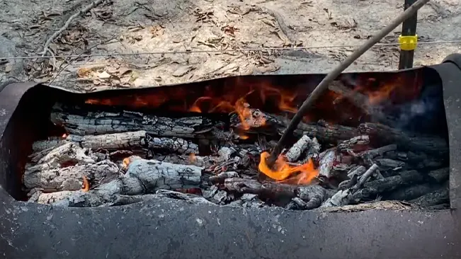 A fire burning in an outdoor grill with a metal poker stirring the embers