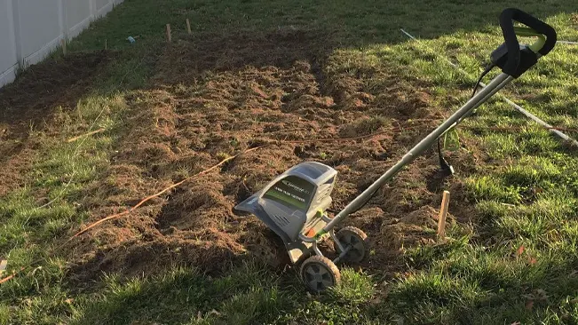 Small, manual garden tiller on freshly tilled soil