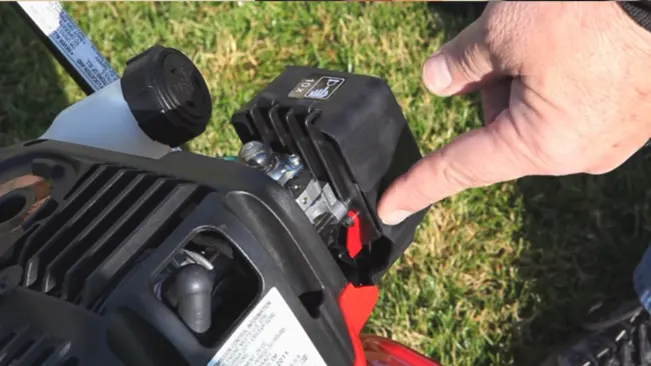 Person pointing at a specific part of a lawnmower’s engine on grass