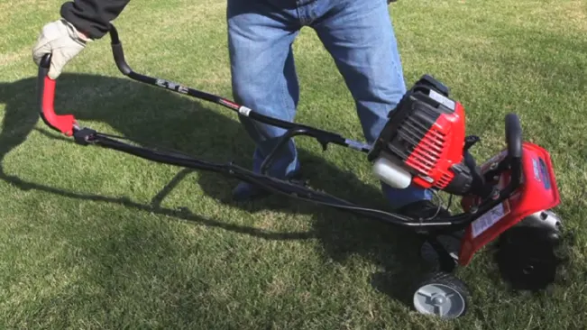 A person using a red and black lawn mower on green grass