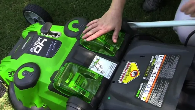 Person’s hands adjusting a green and black lawnmower on grass