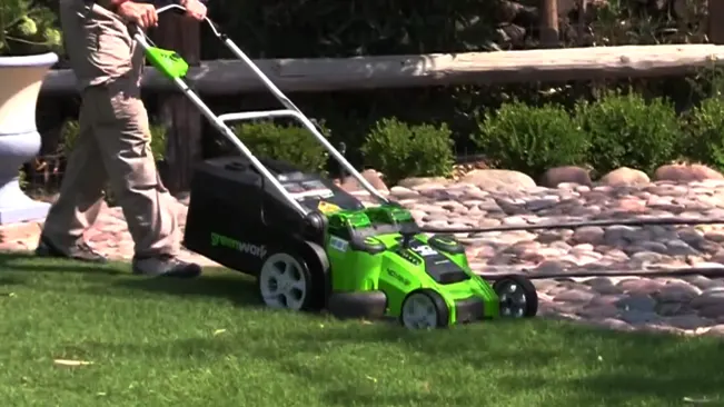 Person using a green and black electric lawnmower in a sunny garden