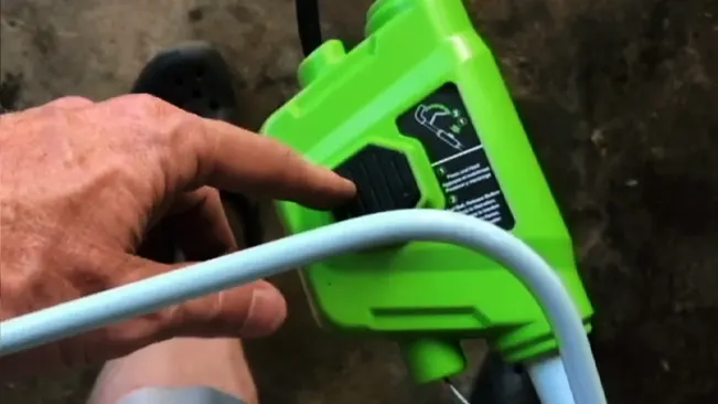 lose-up of a person’s hand operating a bright green power tool with a white electrical cord.