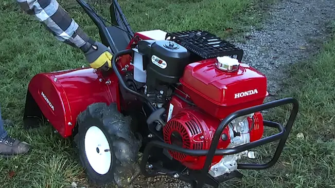 Person operating a red Honda tiller on grassy ground