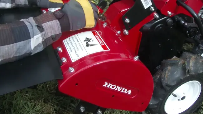 Person in gloves handling a red Honda machinery on grass
