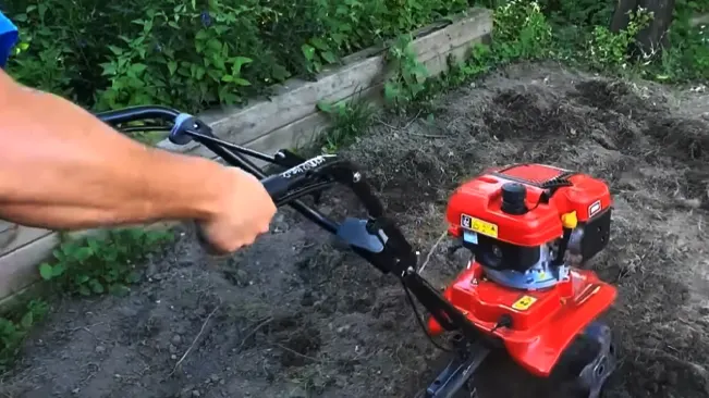 Person operating a red motorized tiller on a patch of soil