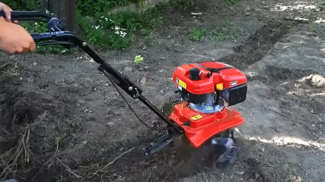 Person operating a mid-sized red tiller on freshly tilled soil