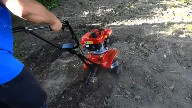Individual operating a red soil tiller in an outdoor setting