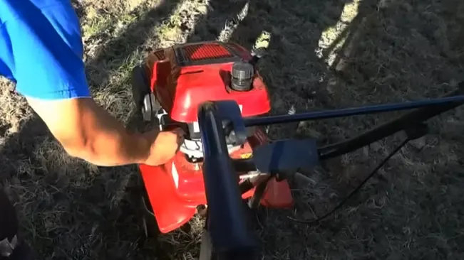 Person in blue operating a red lawnmower on grass