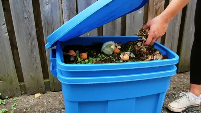 Person adding organic waste to blue compost bin.