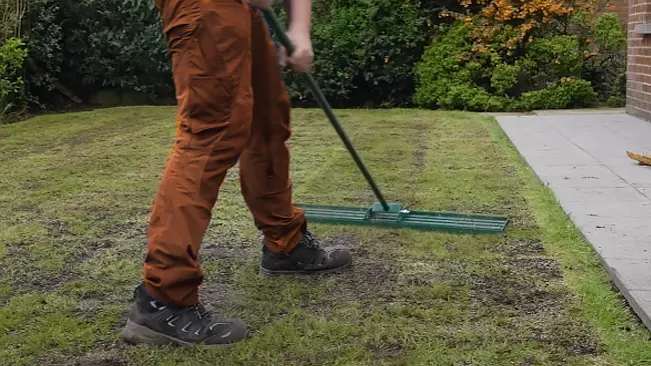 A person in brown pants using a green lawn leveler on a patchy grass area.