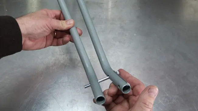 Hands holding two grey, hollow pipes with a small metal rod protruding from one