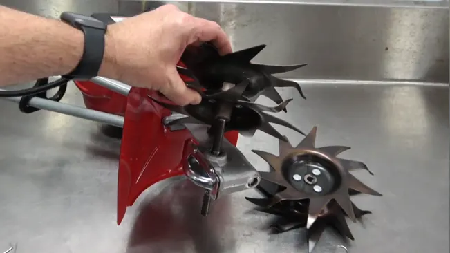 Person cleaning a red and black tiller blade in a sink
