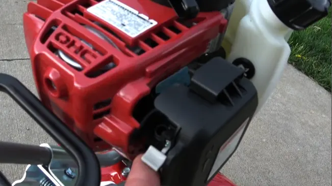 person’s hand pulling the starter cord of a red and black lawnmower engine