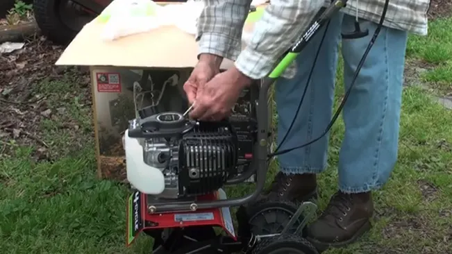 A person in jeans and boots repairing a small engine mounted on a red frame outdoors