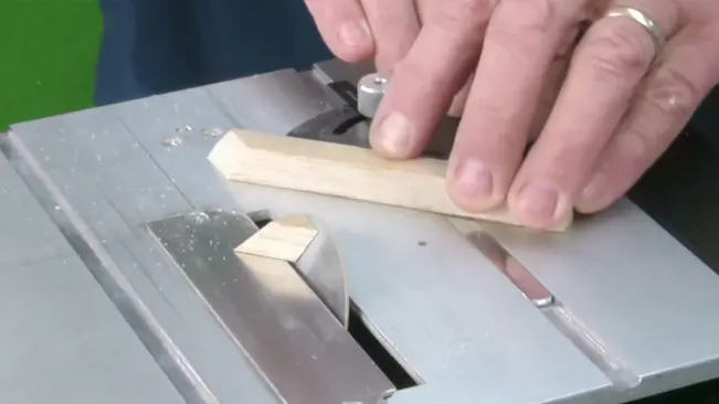 A person using a table saw to cut a piece of wood.