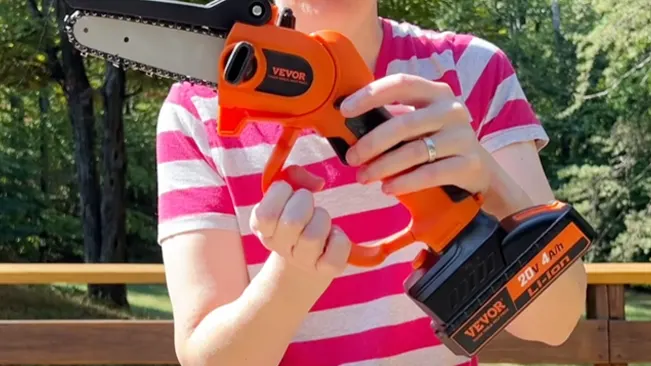 Person holding an orange VEVOR chainsaw outdoors