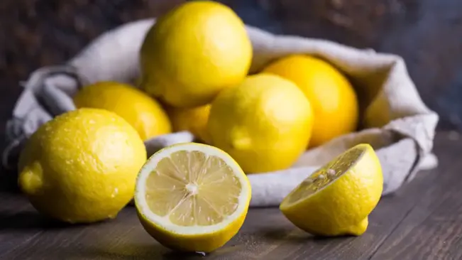 a vibrant display of fresh, ripe lemons on a rustic wooden surface, with one lemon cut in half, showcasing its juicy interior