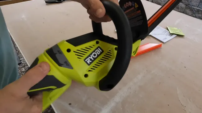 Person holding a green and black RYOBI hedge trimmer above a table