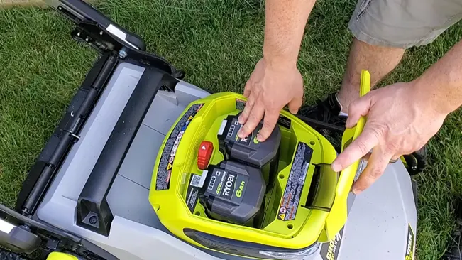 person installing a battery into a green and grey lawnmower