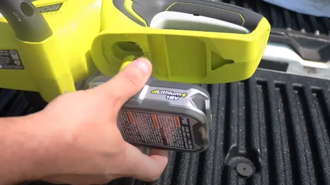 Person inserting an 18V lithium battery into a bright yellow cordless tool on a black ridged surface.