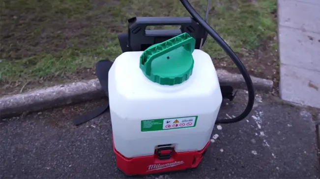 A red and white portable garden sprayer with a green lid on a concrete surface.