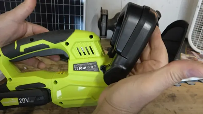 Person holding a bright green and black cordless drill with a 20V battery, in front of a wire grid