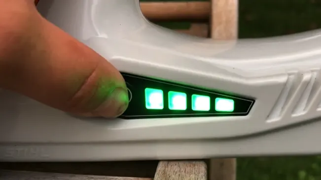 Close-up of a hand adjusting a grey level tool with green illuminated indicators, with a blurred wooden structure in the background