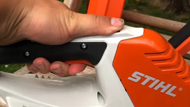 Close-up of a person’s hand gripping a STIHL chainsaw with greenery in the background