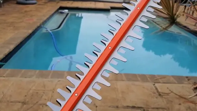 Close-up of an orange and white pool cleaning rake with a swimming pool in the background