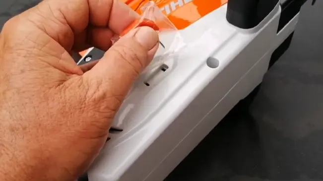 Close-up of a person’s hand peeling off the protective plastic film from a new white appliance with orange details