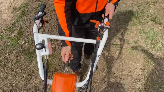 Person in orange and black attire holding a white and orange bicycle outdoors on grassy ground.