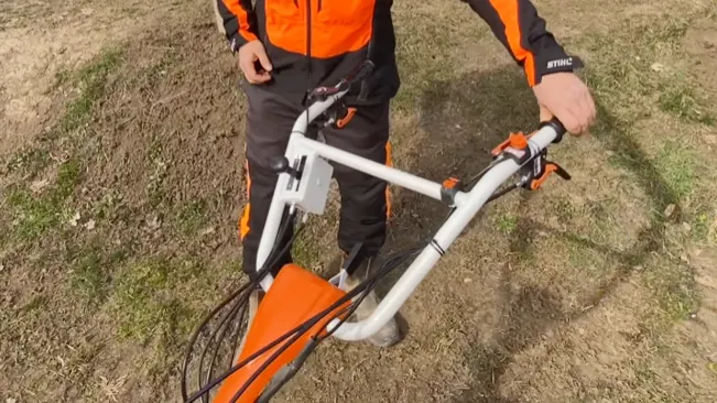 Person in orange and black attire holding a white and orange bicycle on a dirt ground