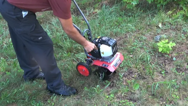 Person operating a red and black garden tiller on grassy soil