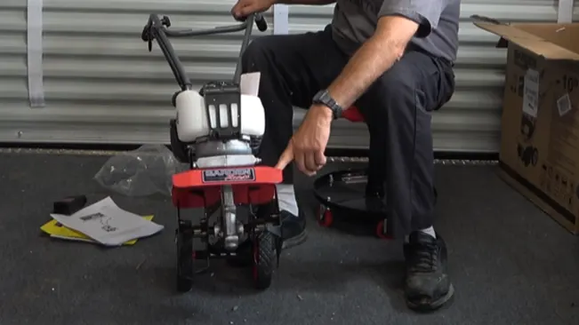  a person seated in a workshop, assembling or repairing a small red and black engine with scattered tools and parts around