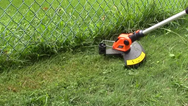 Weed trimmer cutting grass near a fence