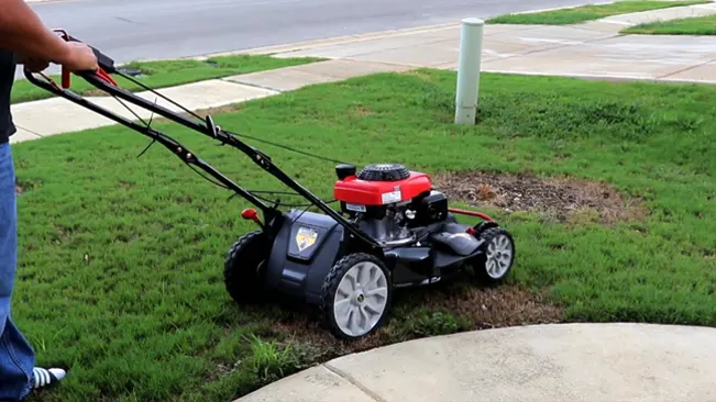 person, from the waist down, pushing a red and black gas-powered lawnmower over a green lawn with some brown spots.