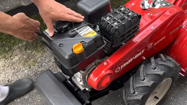 person’s hands inspecting the engine of a red Troy-Bilt Mustang lawnmower