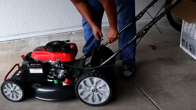person, from the waist down, in blue jeans and sneakers, assembling or checking a red and black lawnmower