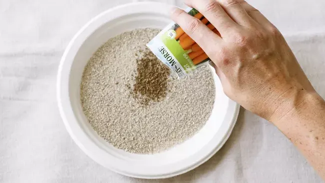 Pouring carrot seeds into a bowl of fine soil mix for planting