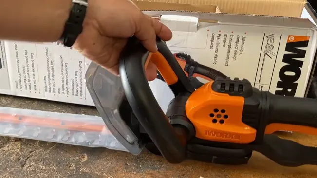 Hand holding a WORX chainsaw with packaging and bubble wrap in the background