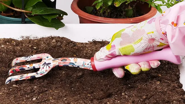 Gardener's hand in a floral glove using a YANZI hand rake on soil