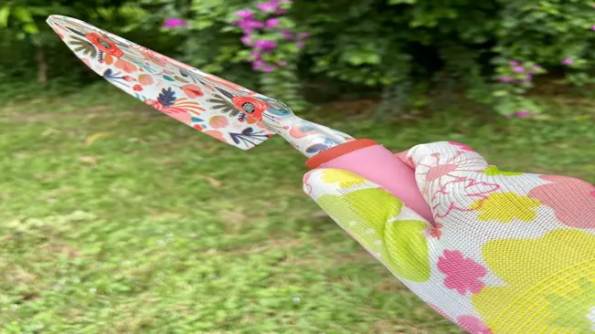 A hand wearing a floral gardening glove holds a YANZI trowel with a matching floral pattern